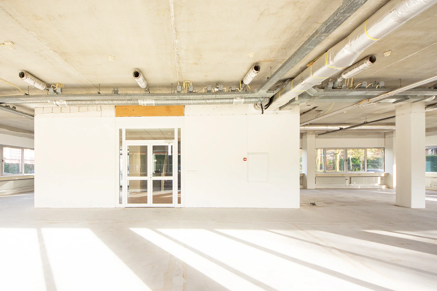 Lichte, lege kantoorruimte aan de Huis-ter-Heideweg met zicht op betonnen plafond en ventilatiebuizen.